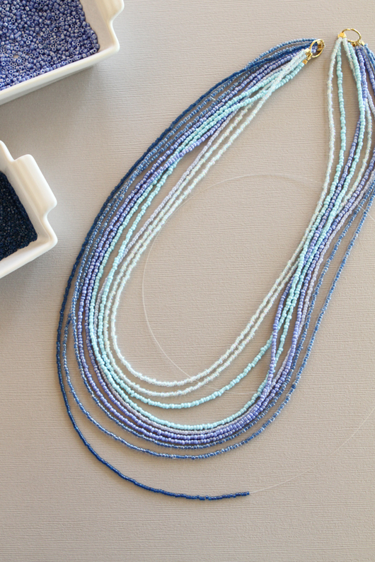 dark blue seed beads being thread onto the necklace wire