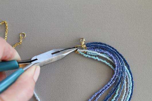 adding the necklace clasp to the jump ring with needle nose pliers