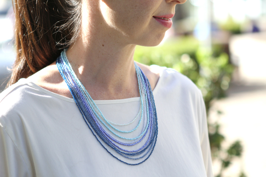 Andrea wearing a white shirt and a blue ombre multi-strand seed bead necklace 