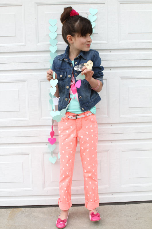 little girl in denim jacket and coral jeans standing in front of white wall