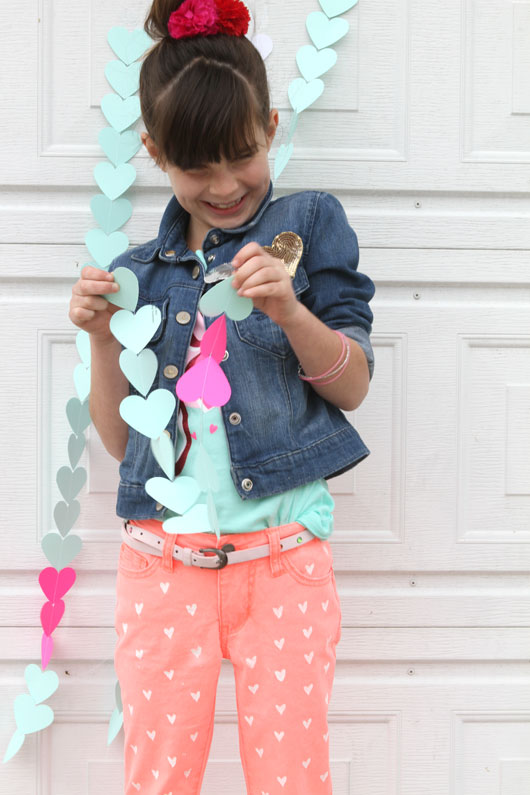 little girl with brown hair giggling next to heart garland