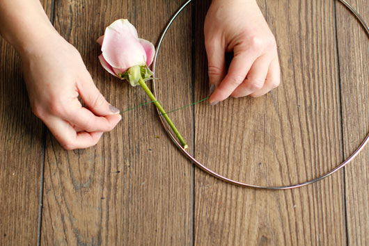 woman attaching flower to metal hoop with green floral wire
