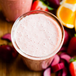 2 glasses filled with strawberry rhubarb smoothie surrounded by sliced fresh fruit