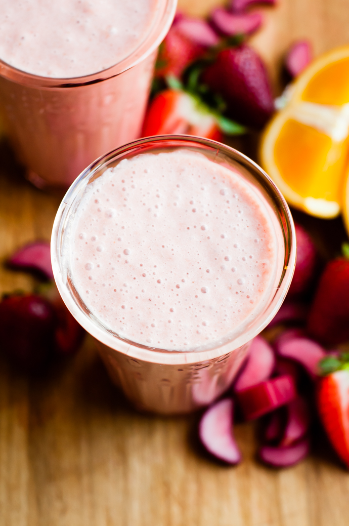 2 glasses filled with strawberry rhubarb smoothie surrounded by sliced fresh fruit