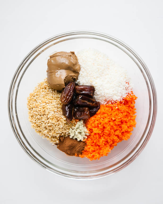 a glass bowl with sunflower butter, dates, cinnamon, vanilla, ginger, coconut, carrots, and cashews