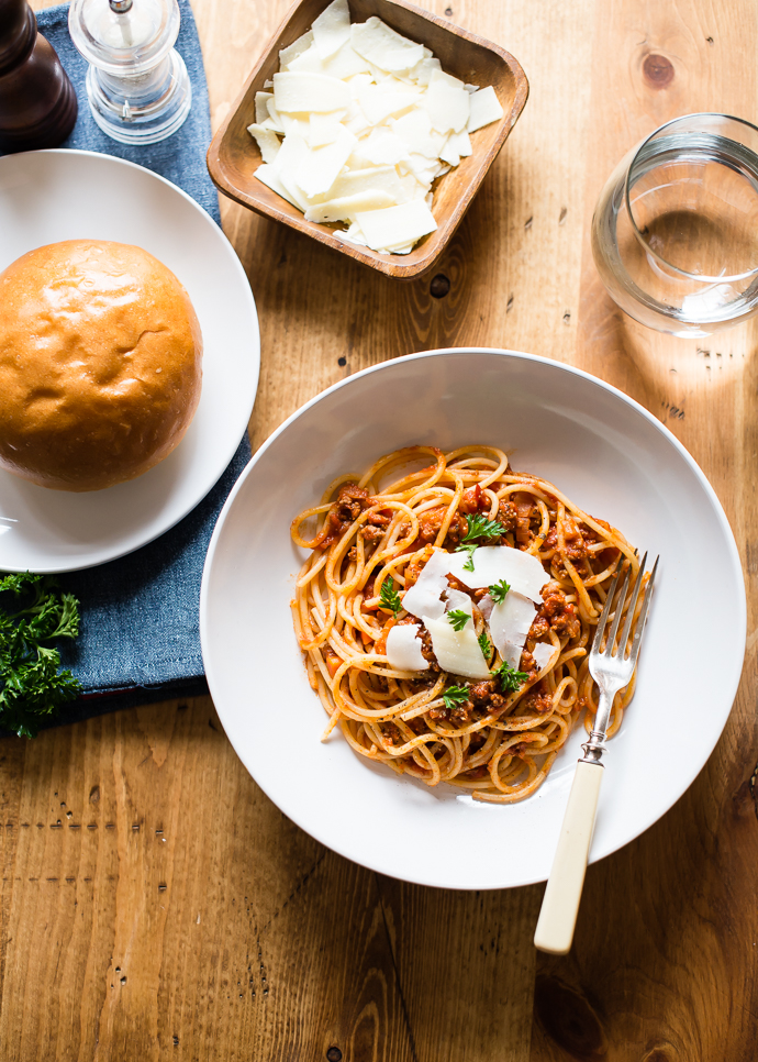 slow cooker tomato sauce with grass fed beef, a bowl of parmesan cheese and glass of water