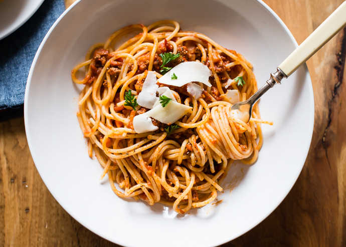 slow cooker tomato sauce with grass fed beef over spaghetti in a white bowl