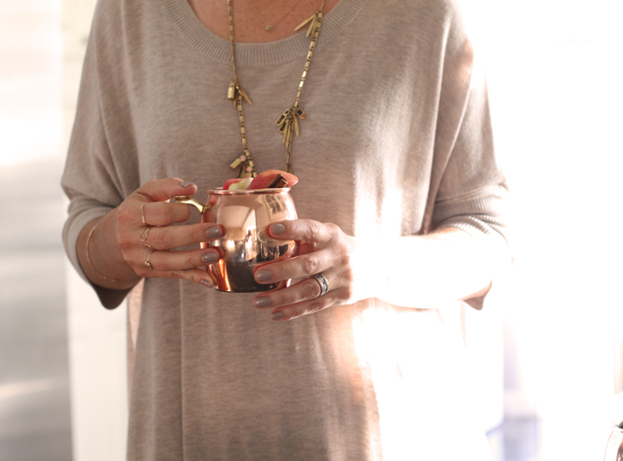 A person in a tan shirt holding an apple cider moscow mule in a copper cup