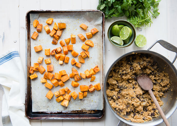 roasted sweet potatoes on a baking sheet, sauce pan of cauliflower rice, and a bowl of limes