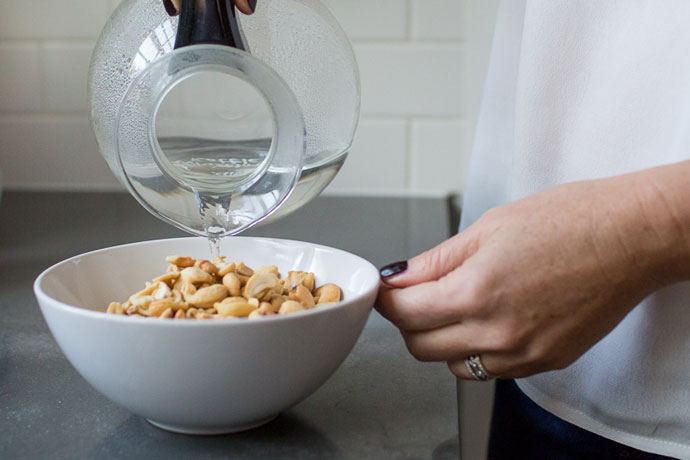pouring water over a white bowl filled with cashews