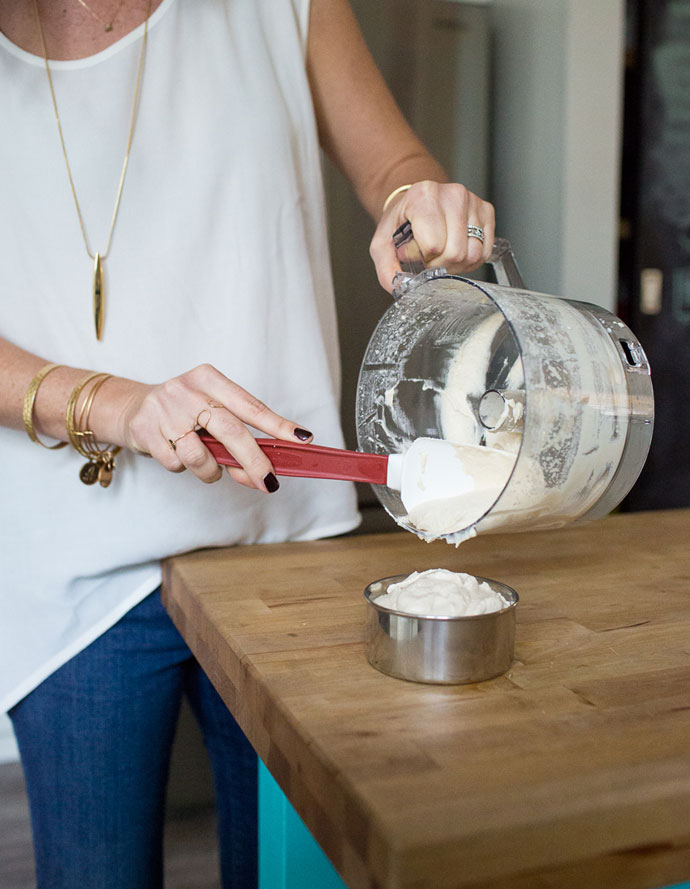 scooping out cashew cream sauce out of food processor into bowl