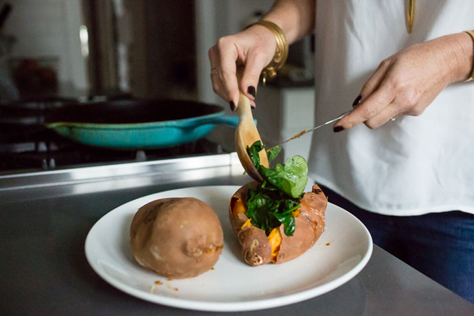 woman spooning sautéed spinach on a sweet potato on a white plate