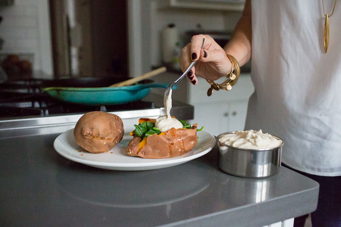 woman spooning cashew cream sauce onto sweet potato on a white plate