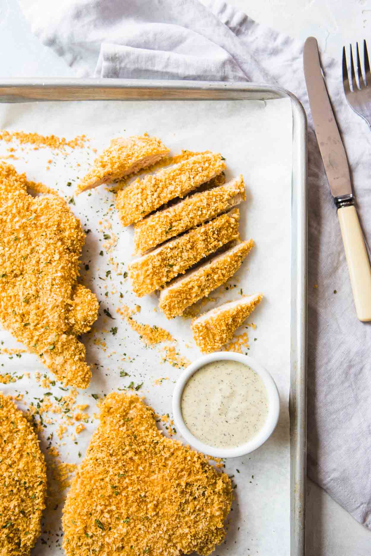 crispy baked chicken cutlets on a baking sheet with ranch dressing