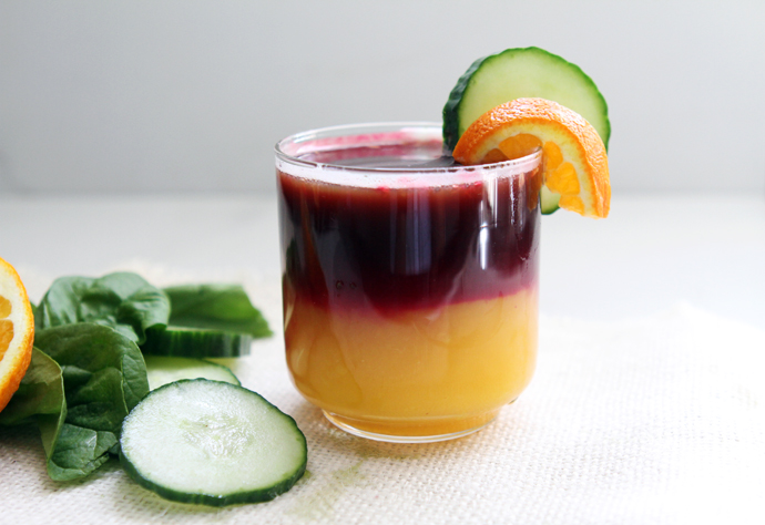 glass of rainbow juice garnished with orange and cucumber slices