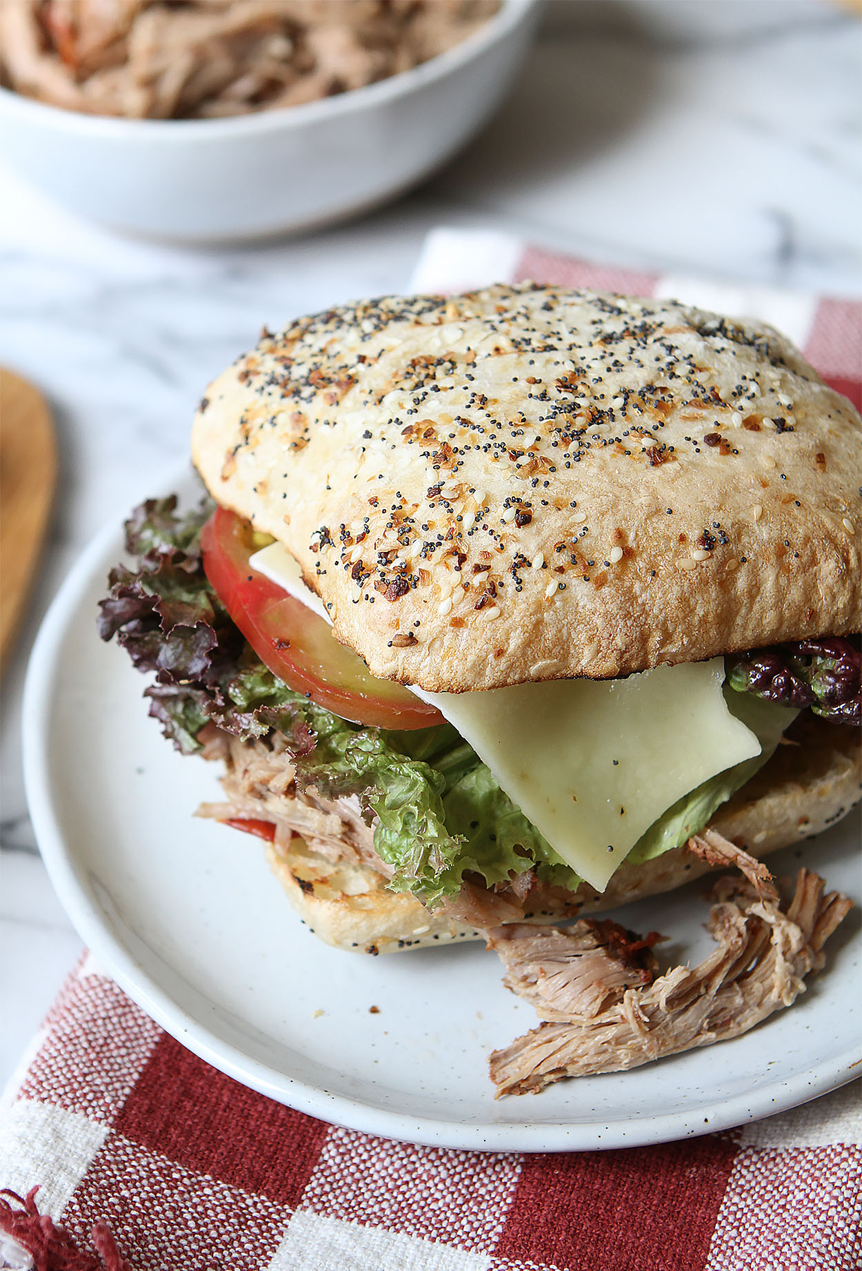 A white plate with easy slow cooker pulled pork on an everything ciabata bun with lettuce ,tomato, and cheese.