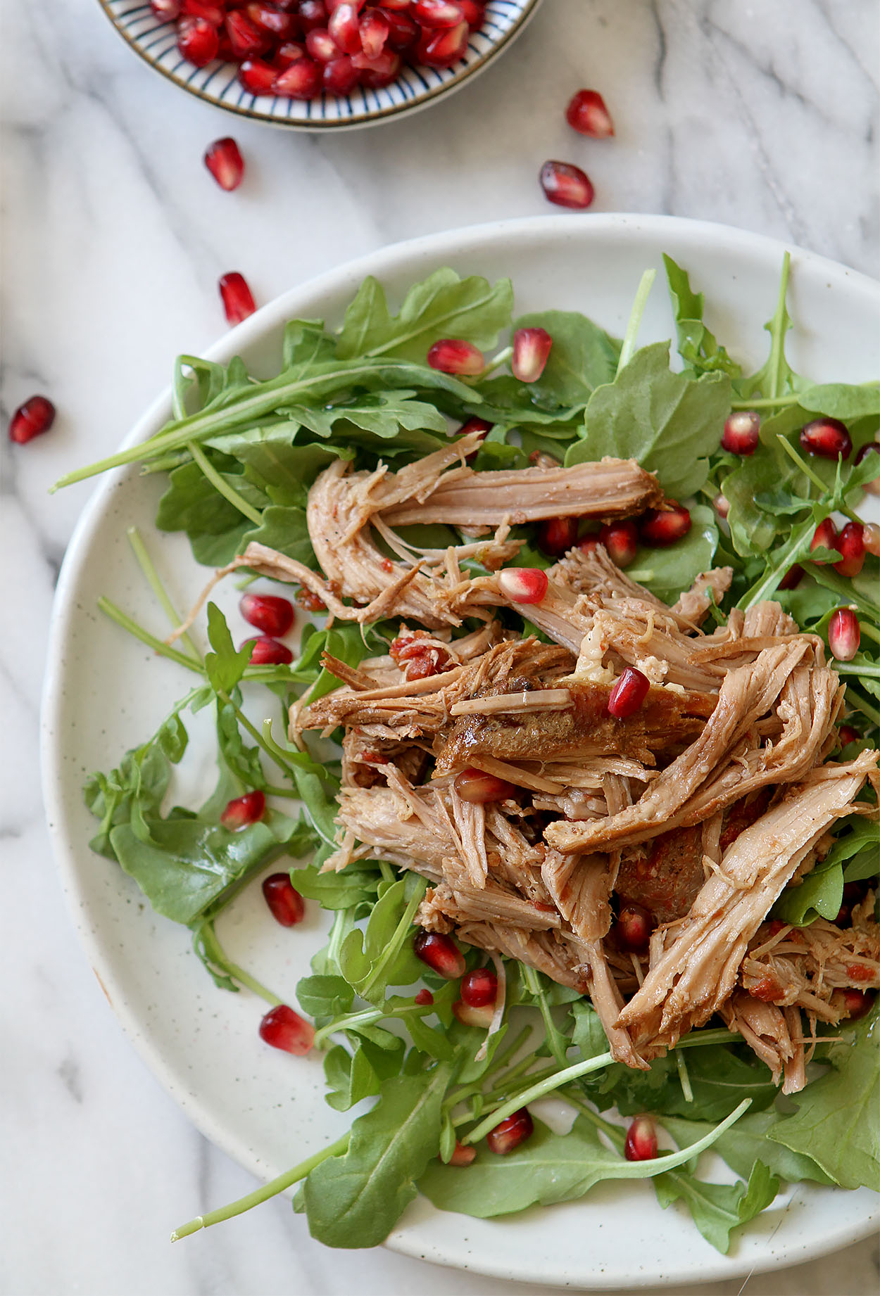 a white plate with arugula pomegranate arils and slow cooker pulled pork