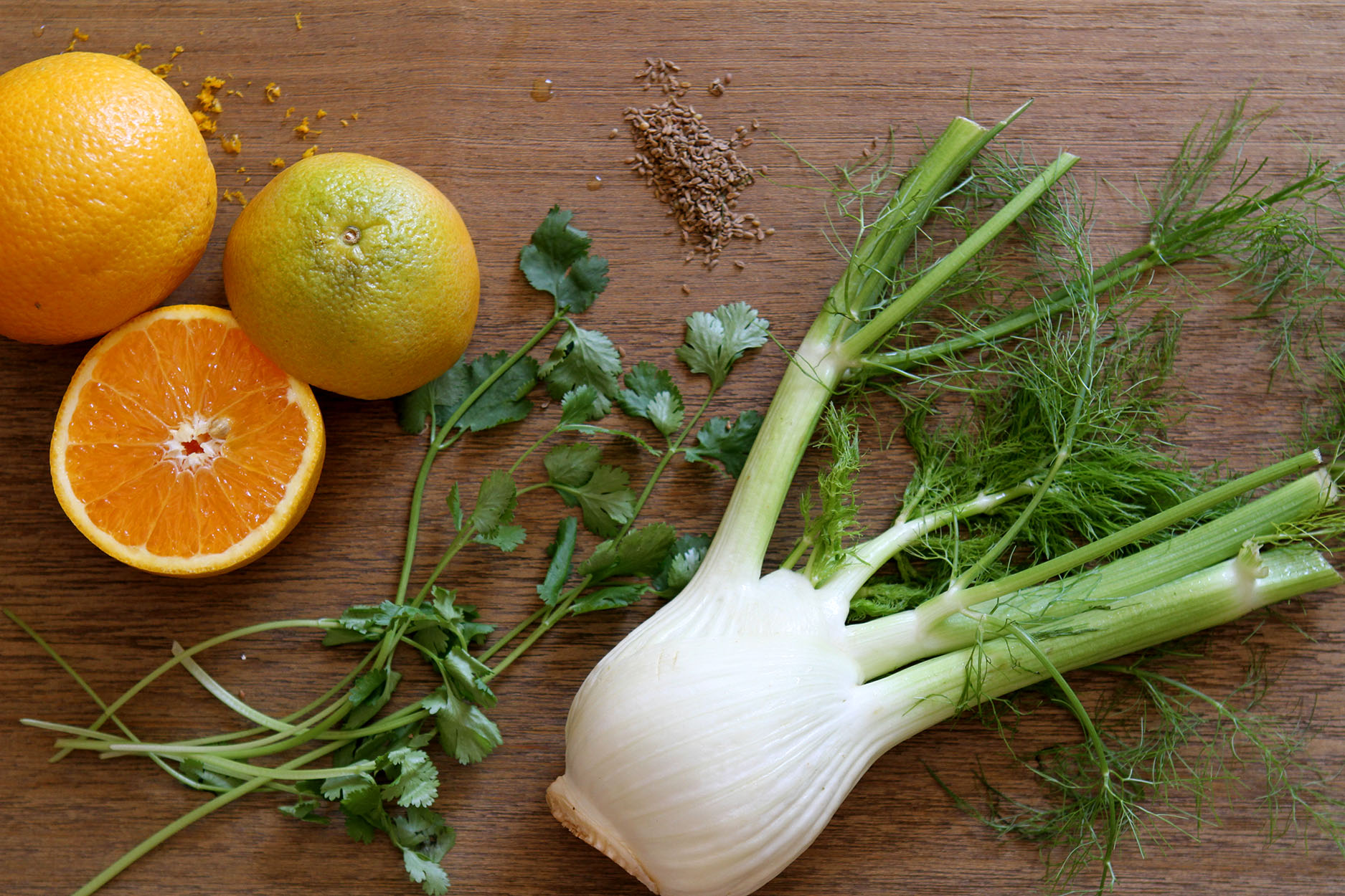 Oranges, parsley, fresh fennel and fennel seeds on a wood cutting board