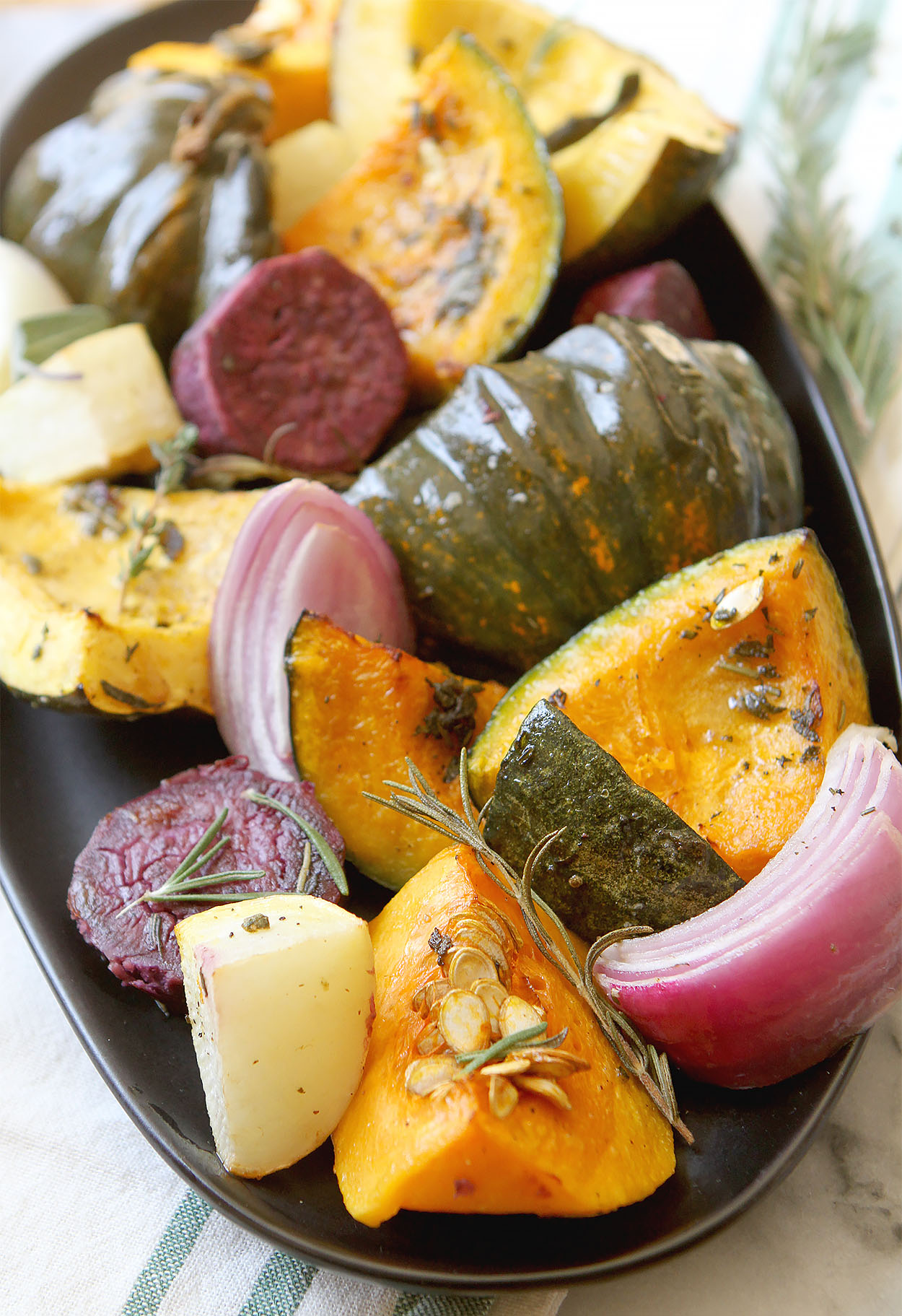 a oblong black plate full of beets, squash, red onions, and sprinkled with rosemary and thyme