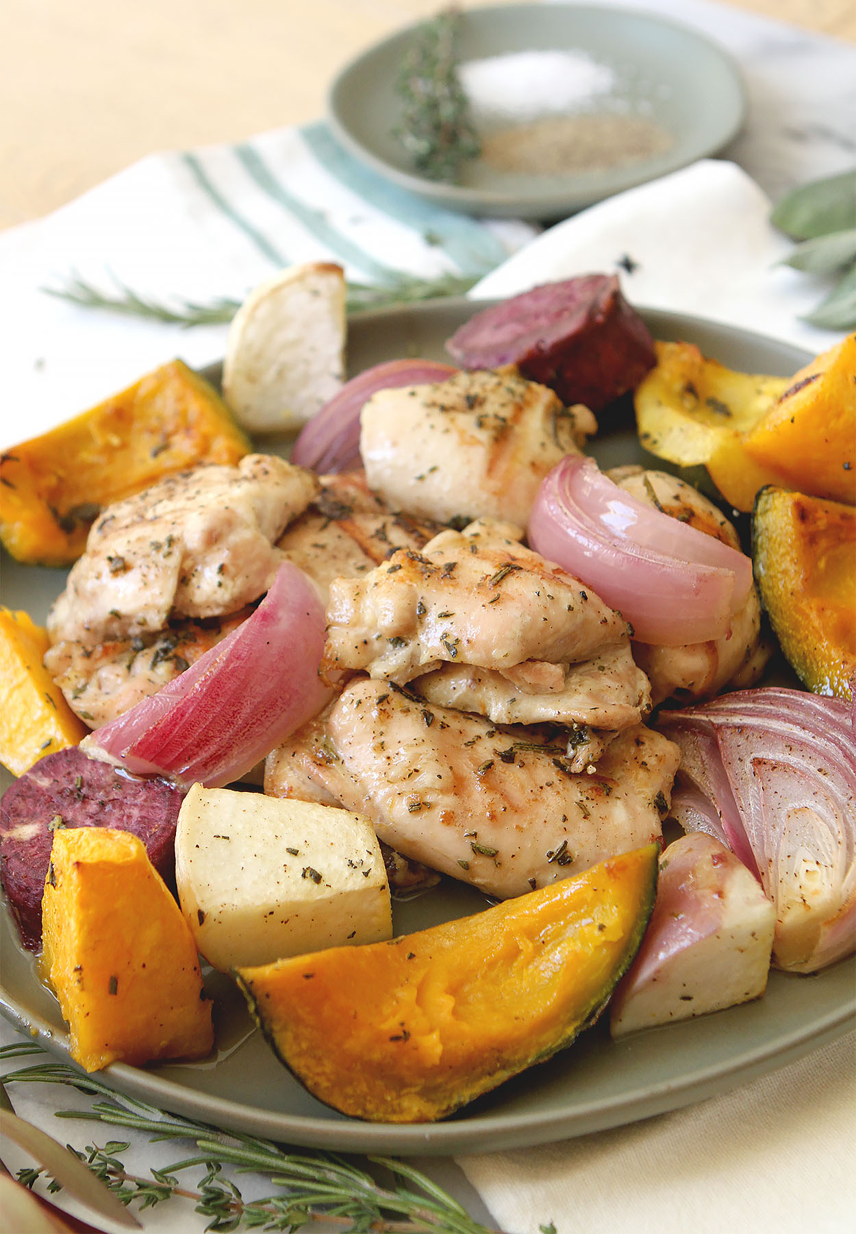 a plate full of chicken, squash, turnips, and red onions. Salt, pepper and thyme on a round plate in the background