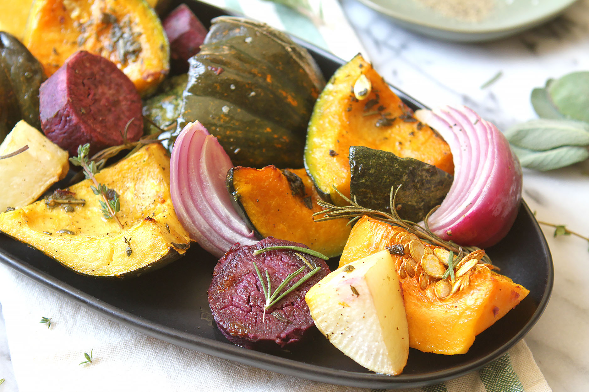 an oblong black plate full of squash, beets, red onions, turnips, and sprinkled with rosemary and thyme