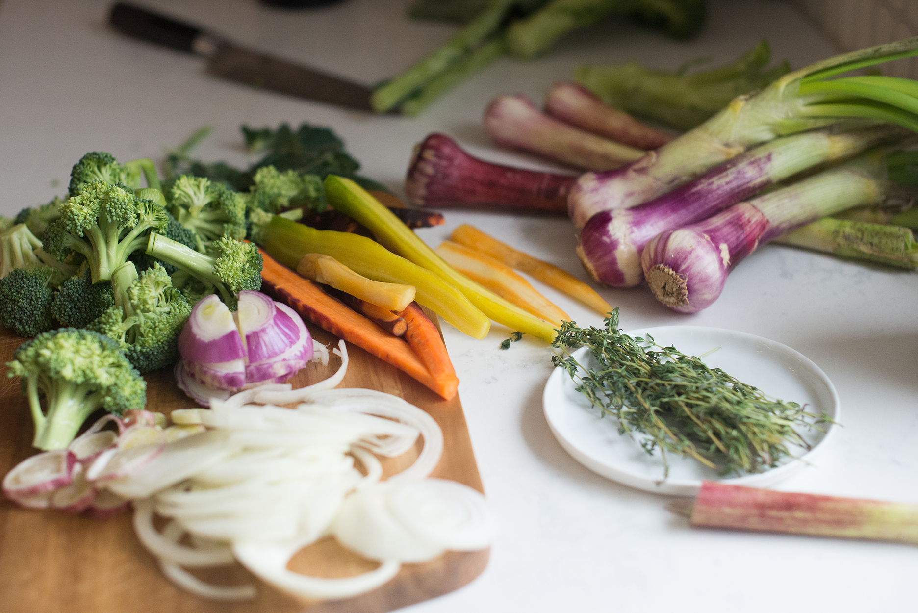 fresh broccoli, red onions, green garlic, carrots and thyme on a wooden cutting board
