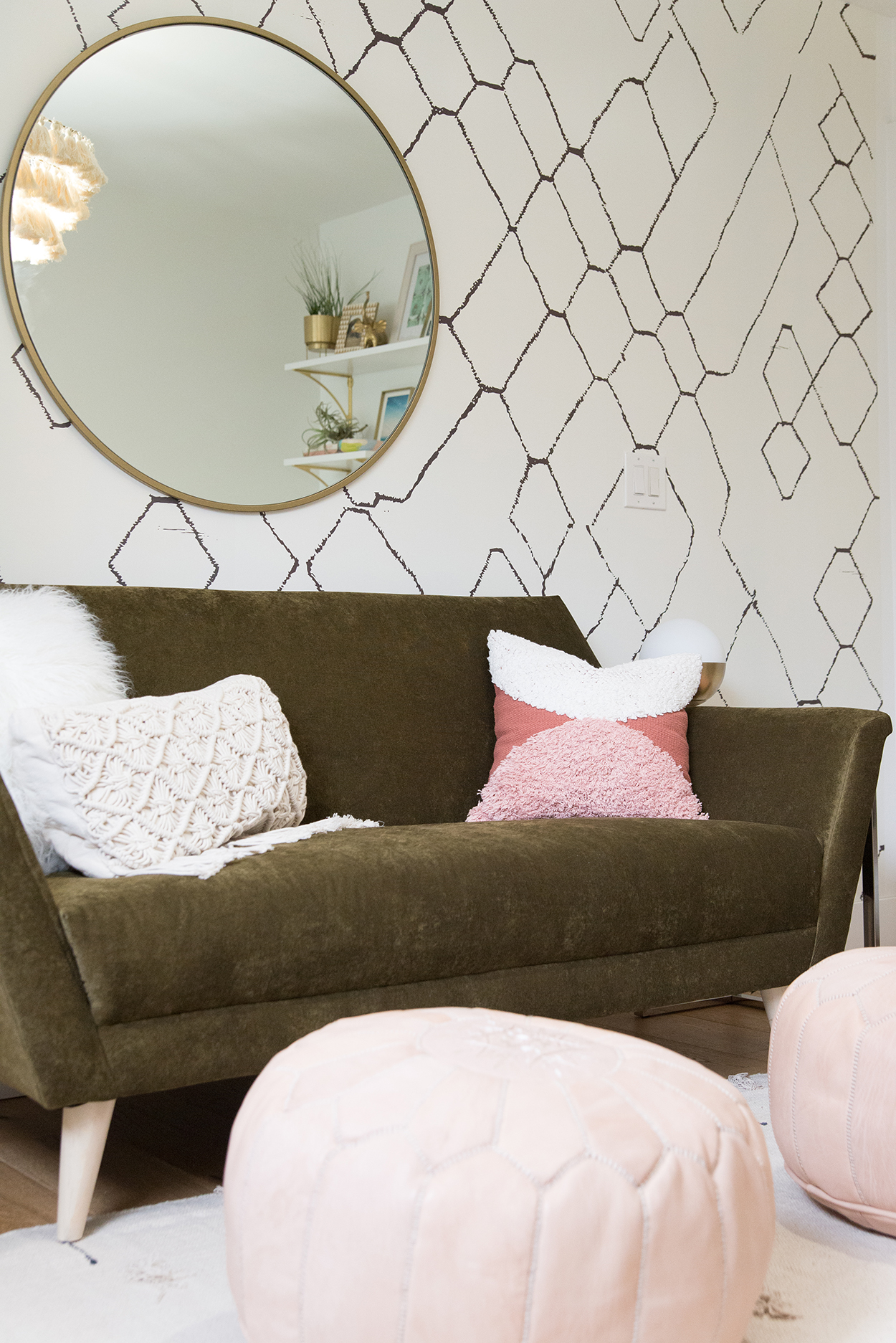 A geometric wallpapered wall with round mirror and a green couch 