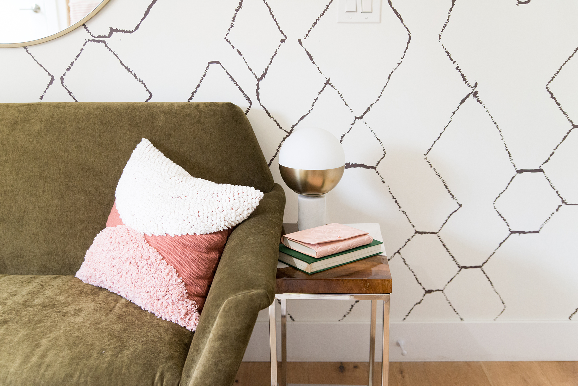 a neutral colored couch with a pink pillow and a side table sitting in front of a wall with geometric wallpaper