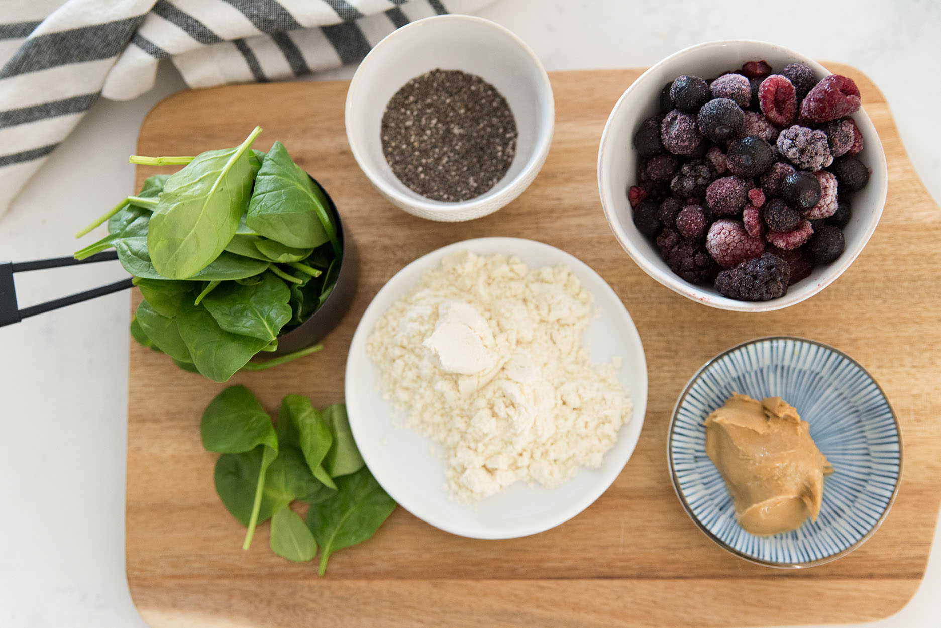 a cutting board with chia seeds, frozen fruit, protein powder, peanut butter and spinach