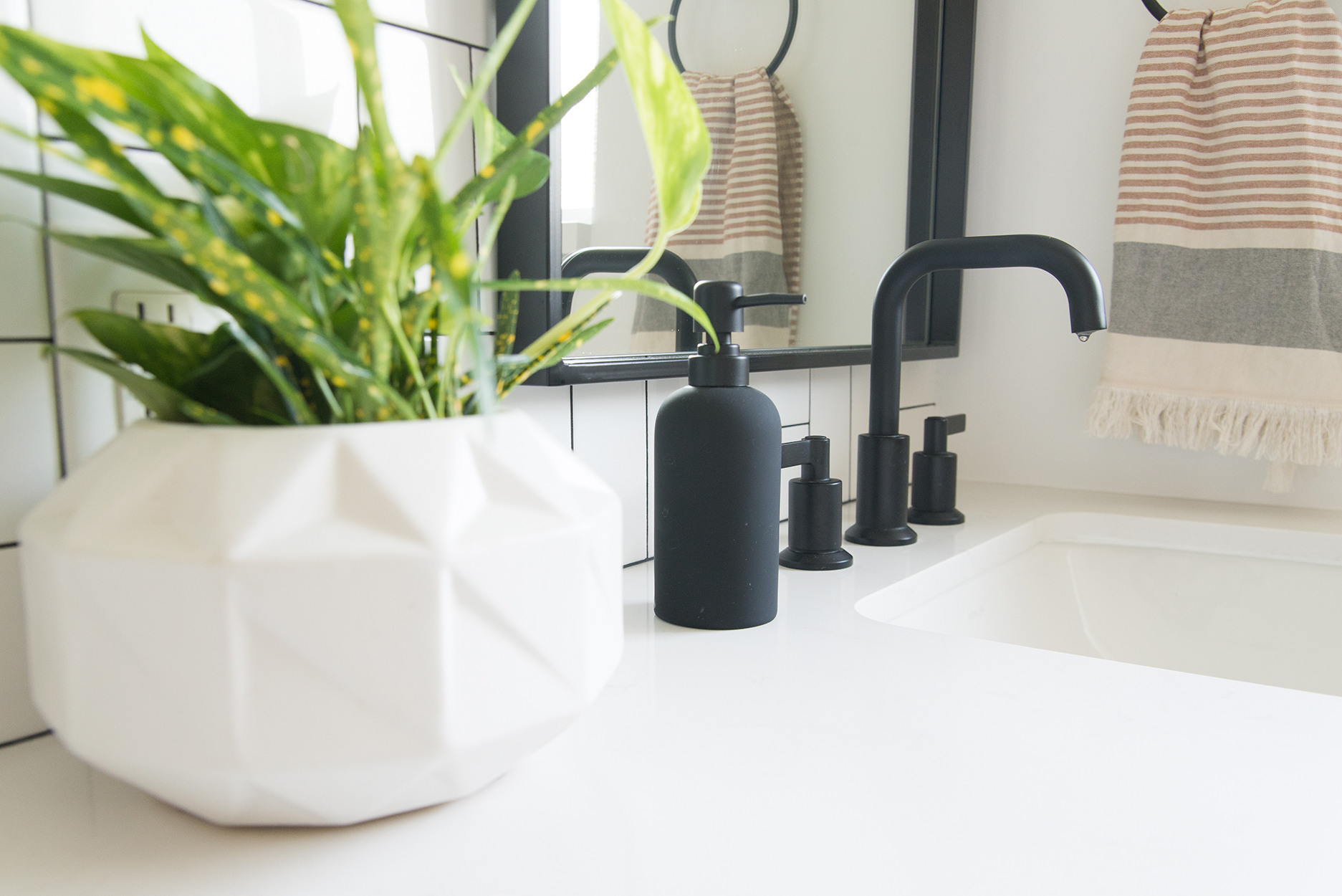 white bathroom vanity counter top with black fixtures and a white vase with a green plant