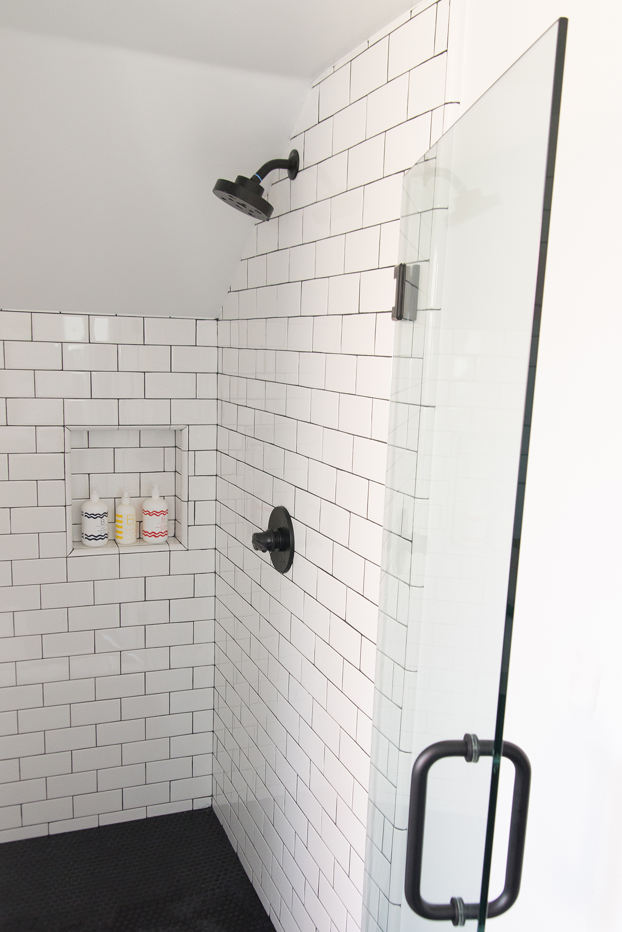 shower with a glass door and white tile and a black tile floor