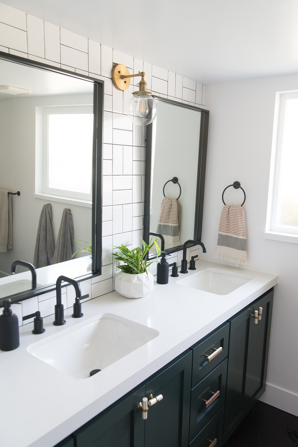 black bathroom vanity with a white counter top and black fixtures, black mirrors and a white tiled wall