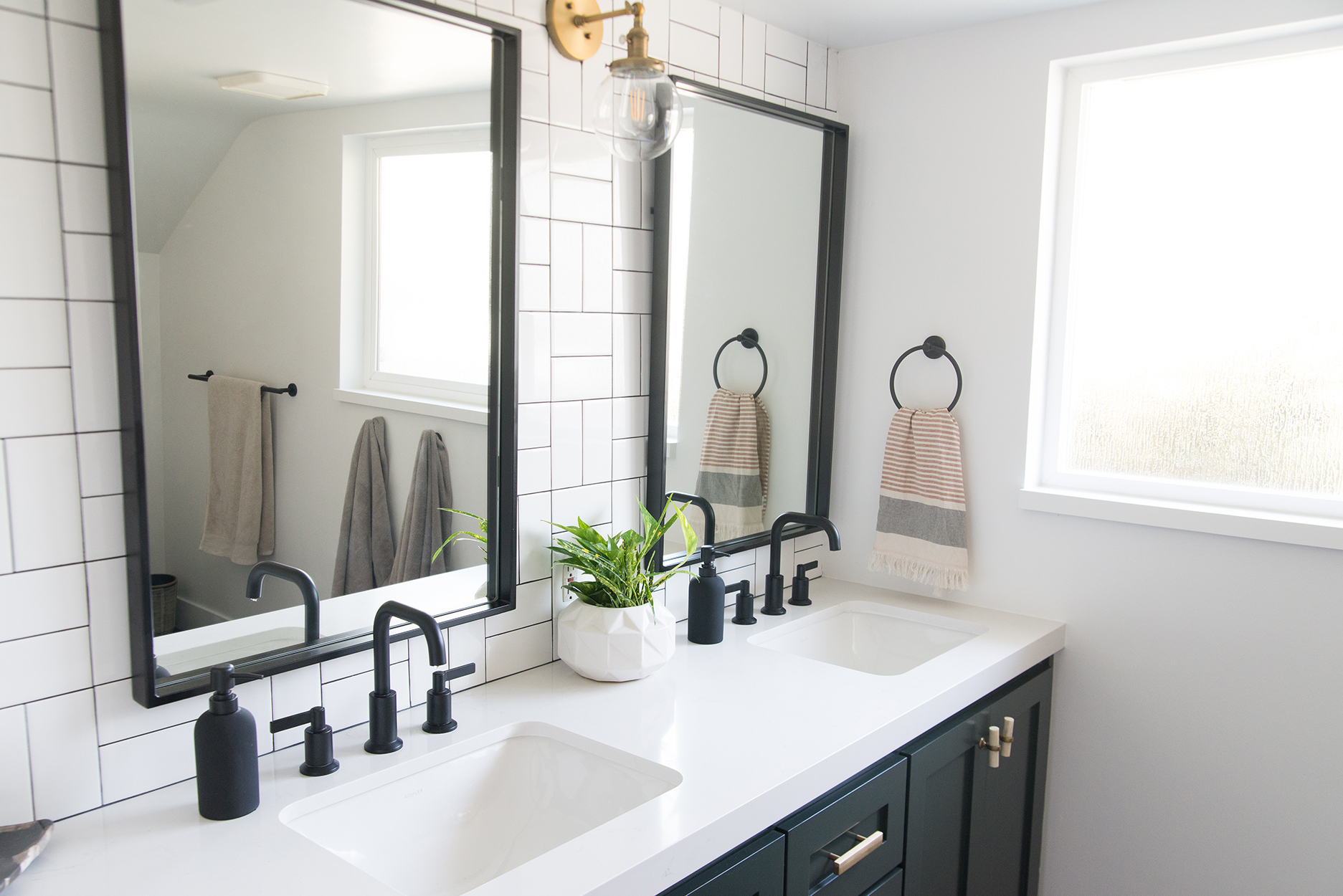 white counter top with black fixtures and black mirrors on a white tiled wall