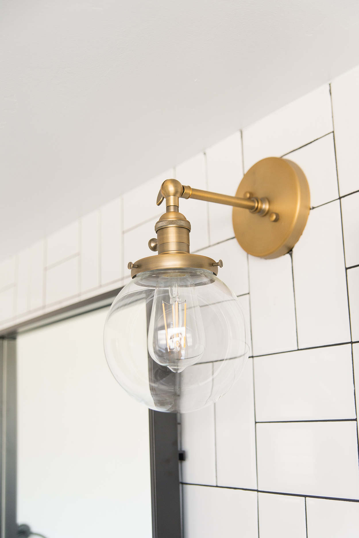 Antique brass light fixture with globe glass and an Edison bulb on a white tiled wall