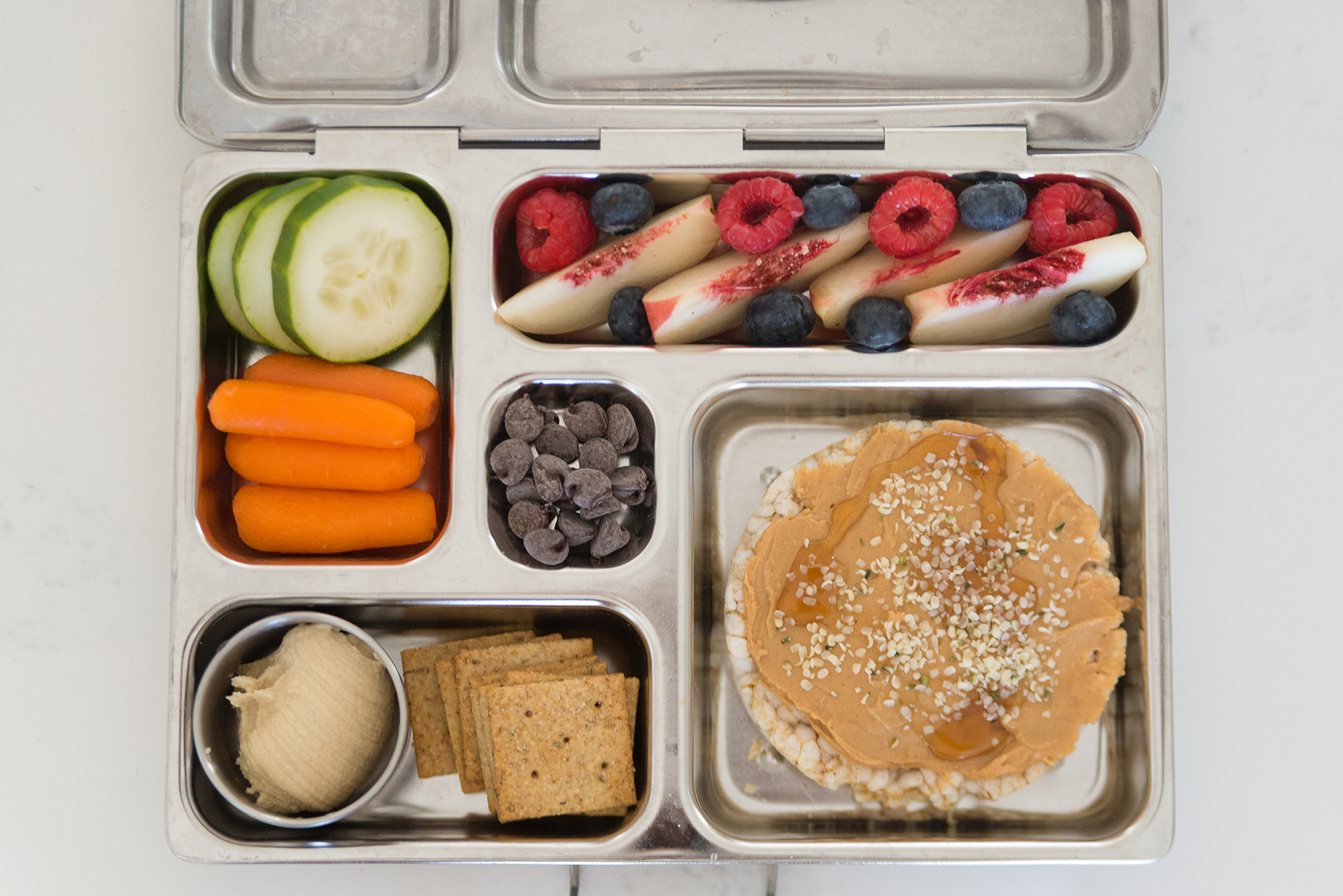 bento box full of fruit, veggies, hummus and a peanut butter rice cake