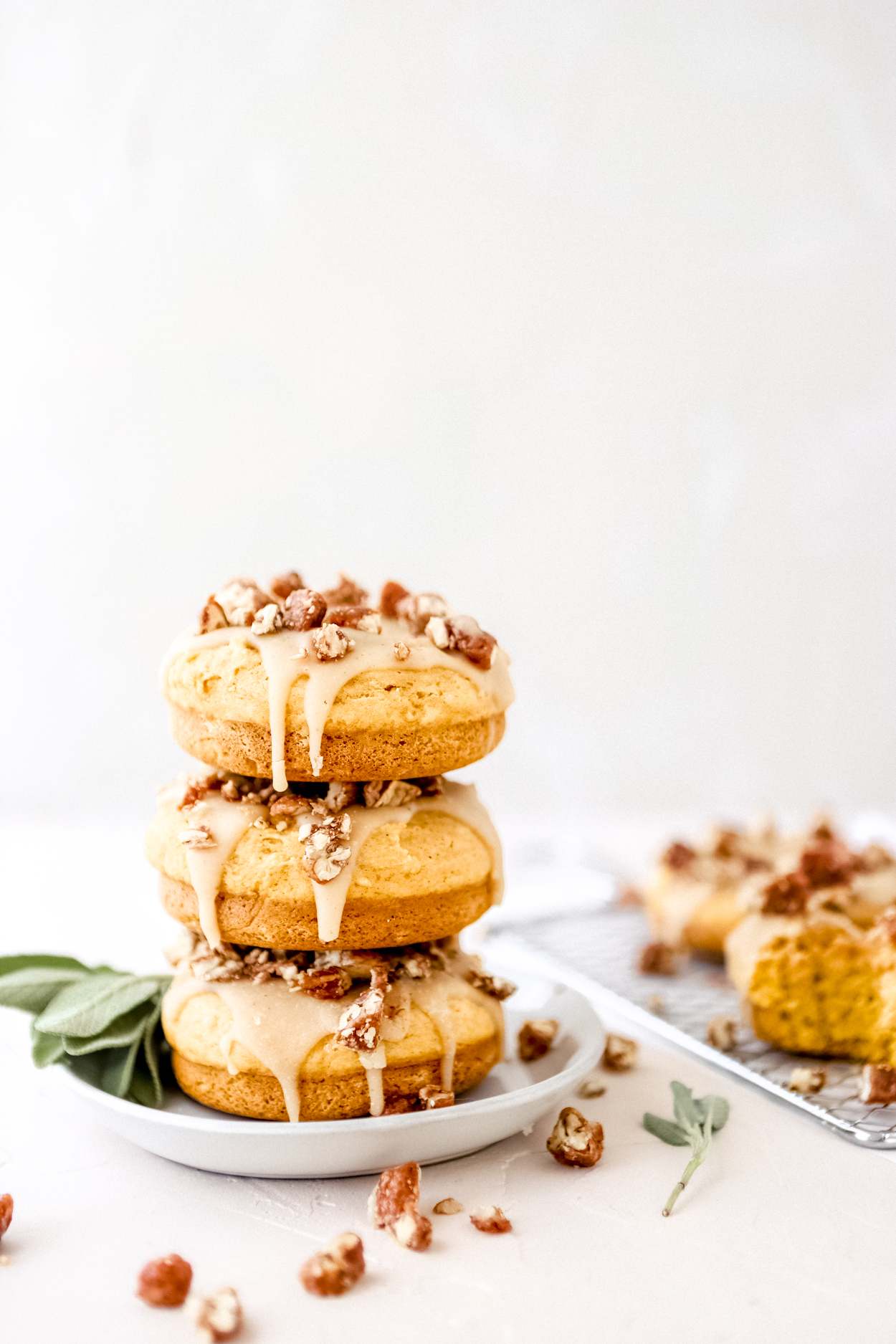 A stack of Baked Pumpkin Donuts on a round white plate, sage to the side