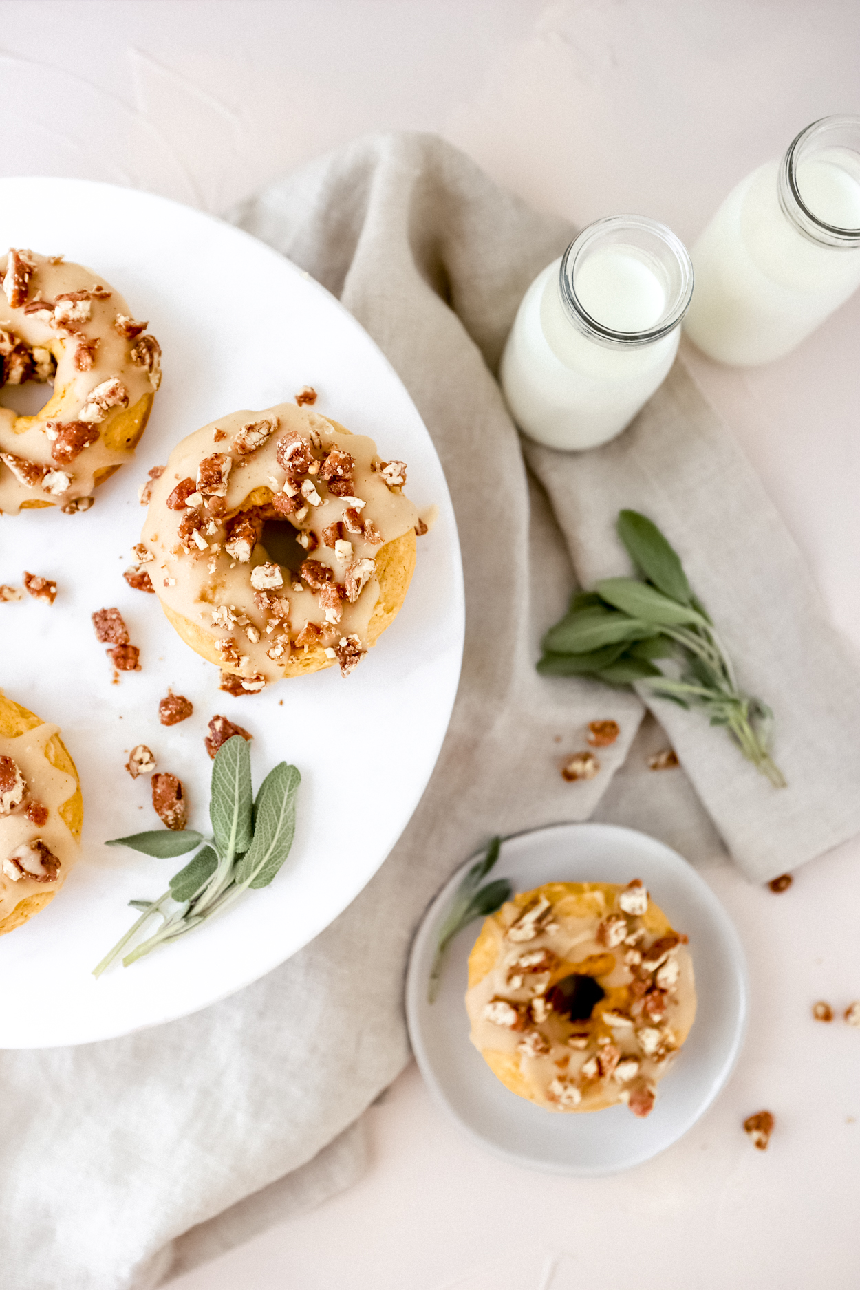 Baked Pumpkin Donuts topped with glaze and pecans on a white plate, glass jars of milk to the side