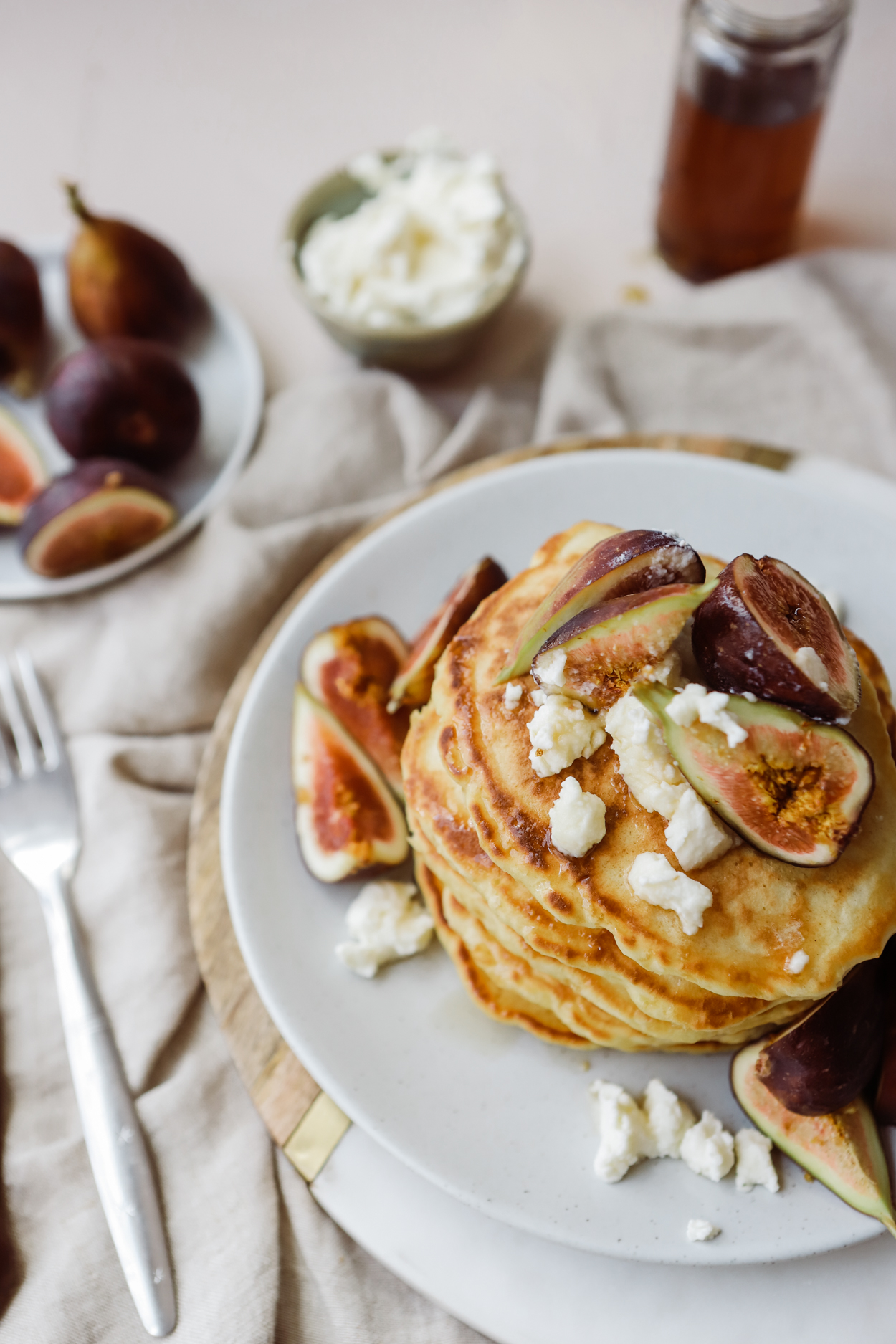 A stack of everyday pancakes on a white plate topped with fresh figs and ricotta cheese, drizzled with honey