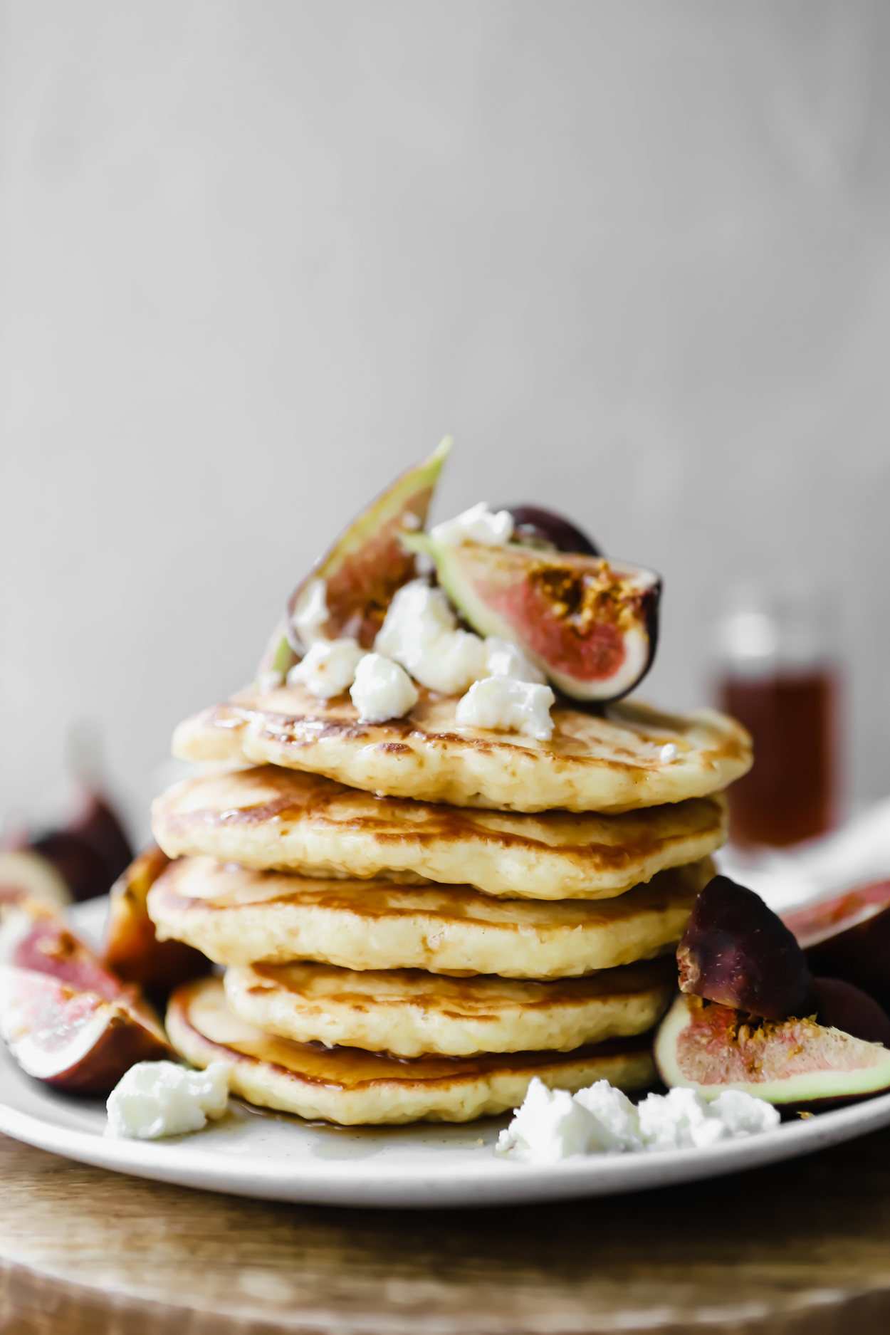 A stack of homemade fluffy pancakes on a plate with fresh figs and ricotta cheese