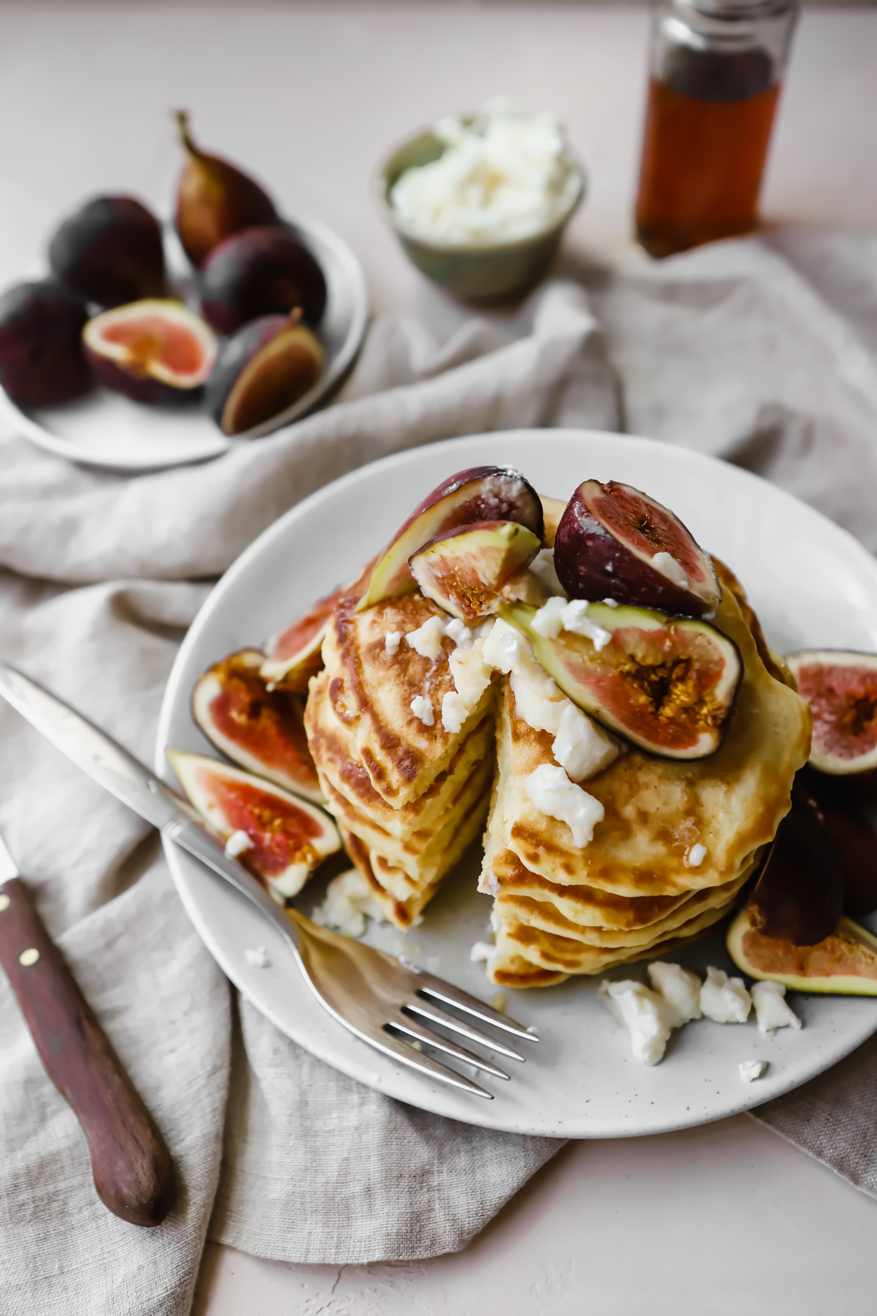 A stack of basic pancakes topped with fresh figs and ricotta cheese, with a slice cut out 