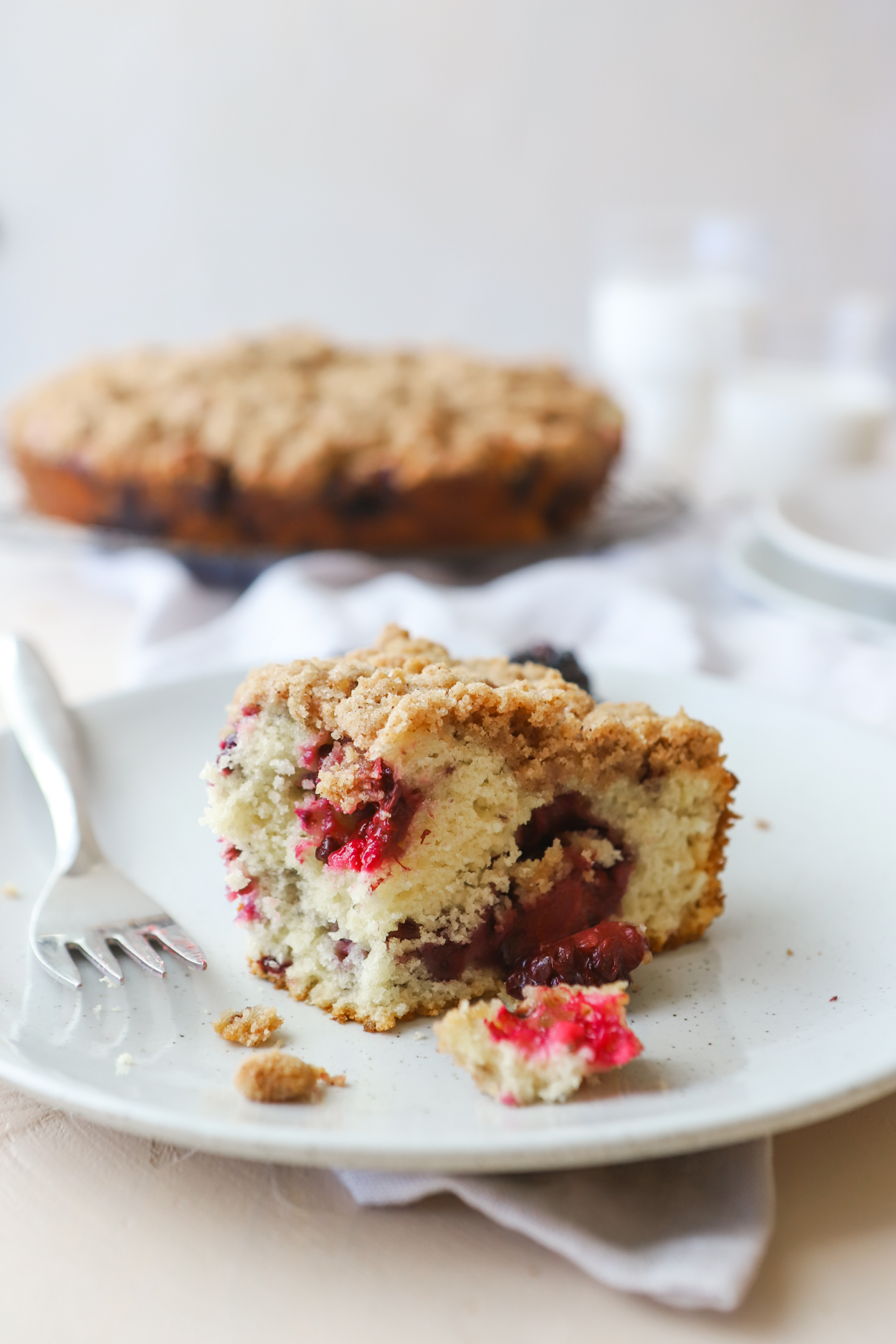 Slice of Blackberry Cake on a gray plate with a fork on a white background