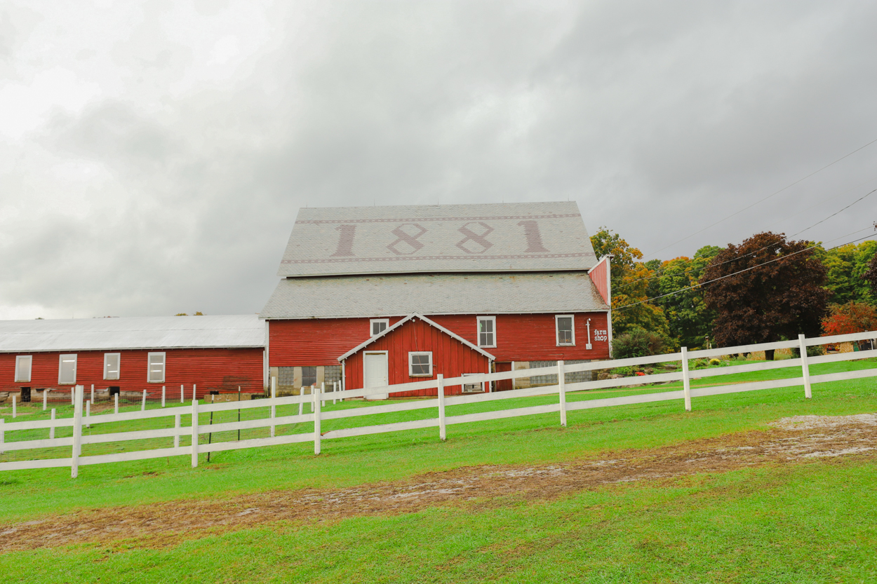 Red barn with tiled roof marked 1881 in green field with white wooden fence in Vermont