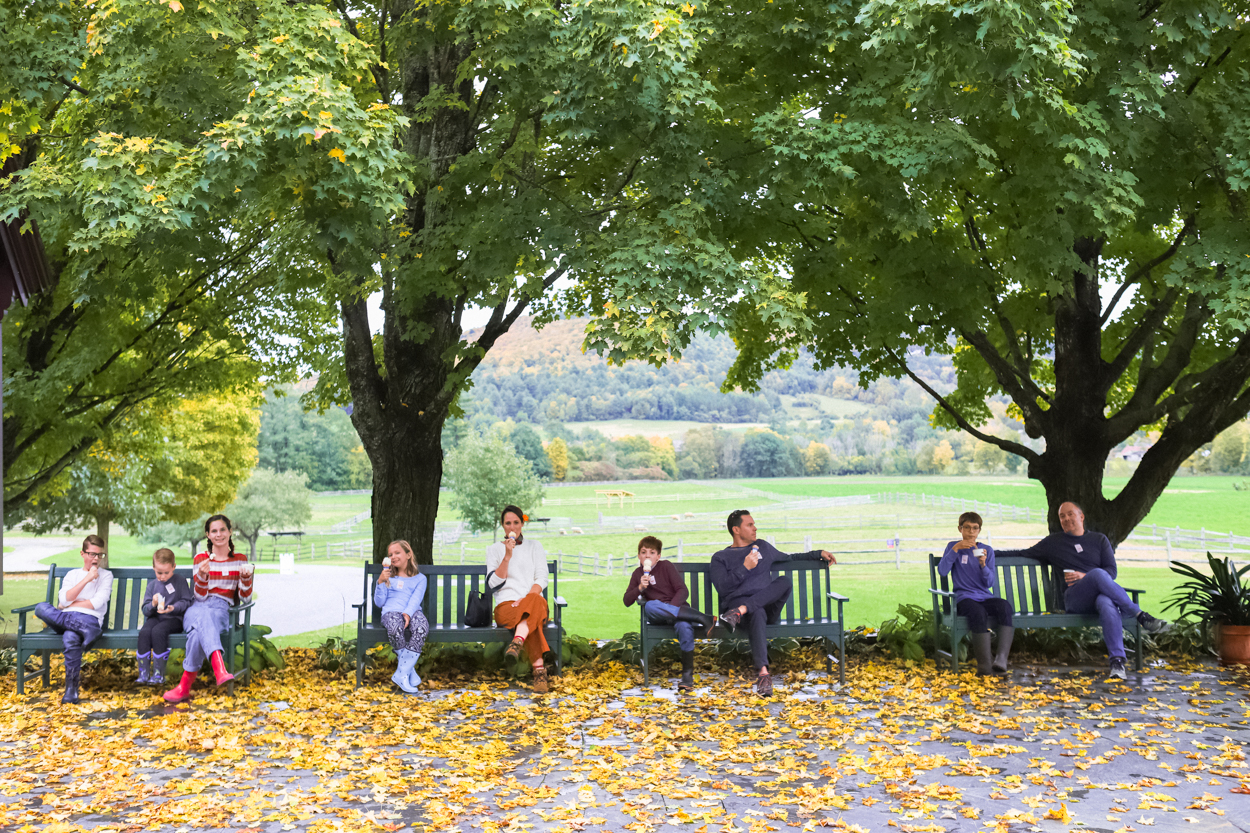 Group of people sitting on benches eating ice cream in front of green trees and yellow leaves