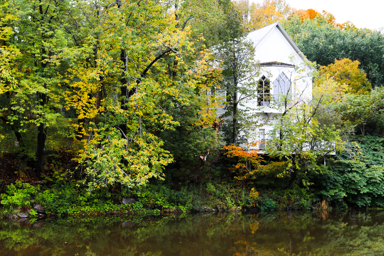 White farmhouse on the sore of a river in Vermont during the Fall 