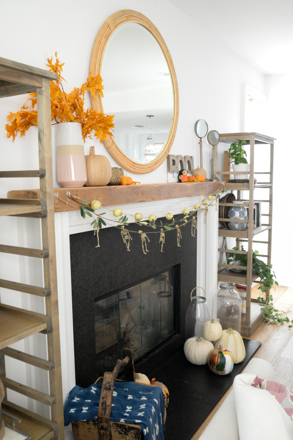 Skull and skeleton garland hanging from a wood beamed mantel with orange leaves and pumpkins and round mirror