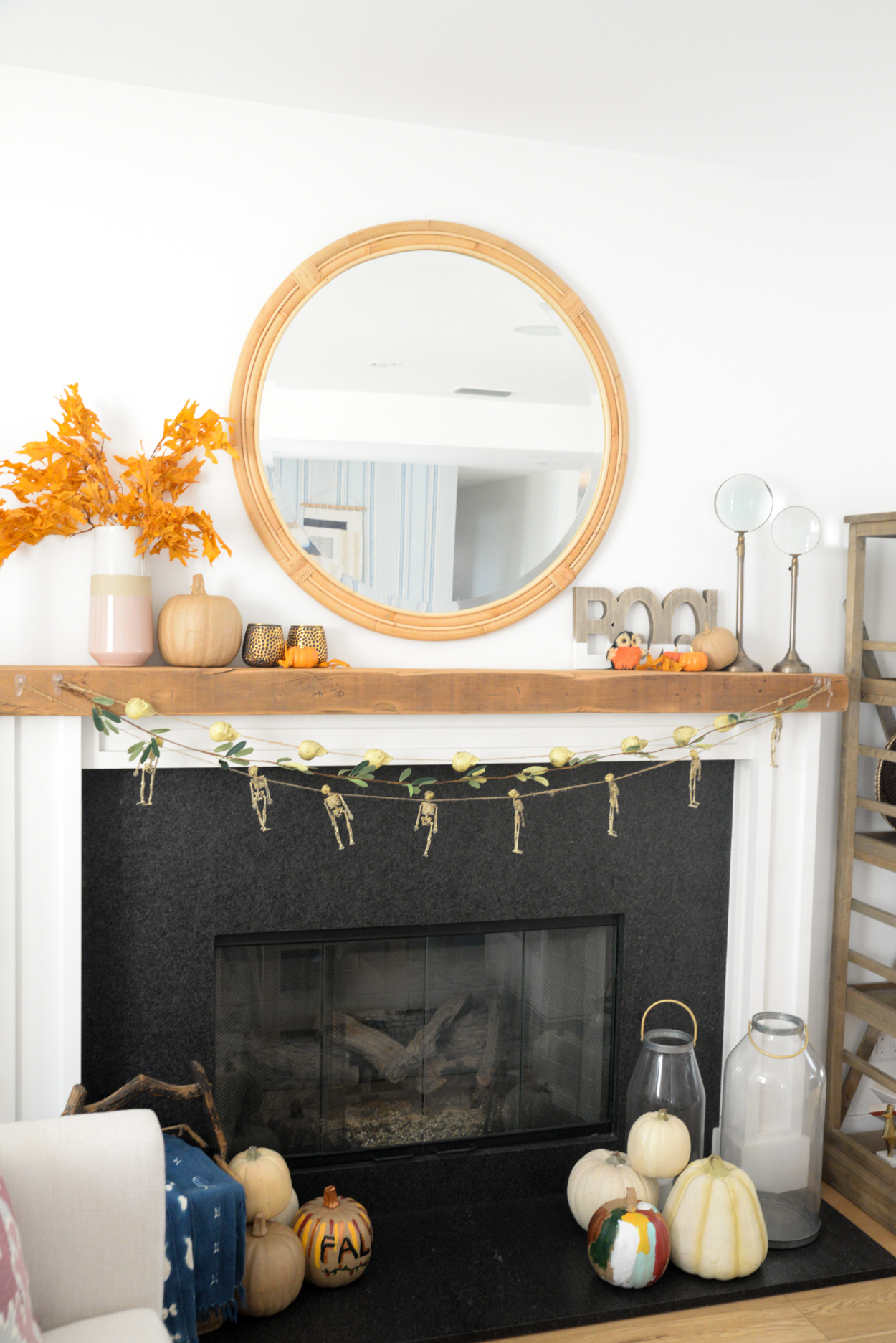 Skull and skeleton garland hanging from a wood beamed mantel with orange leaves and pumpkins and round mirror