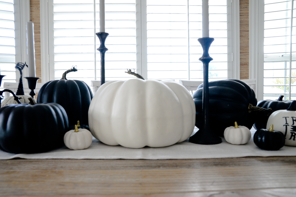 Black and white pumpkins and black candlesticks sitting on a rustic wood farmhouse dining table