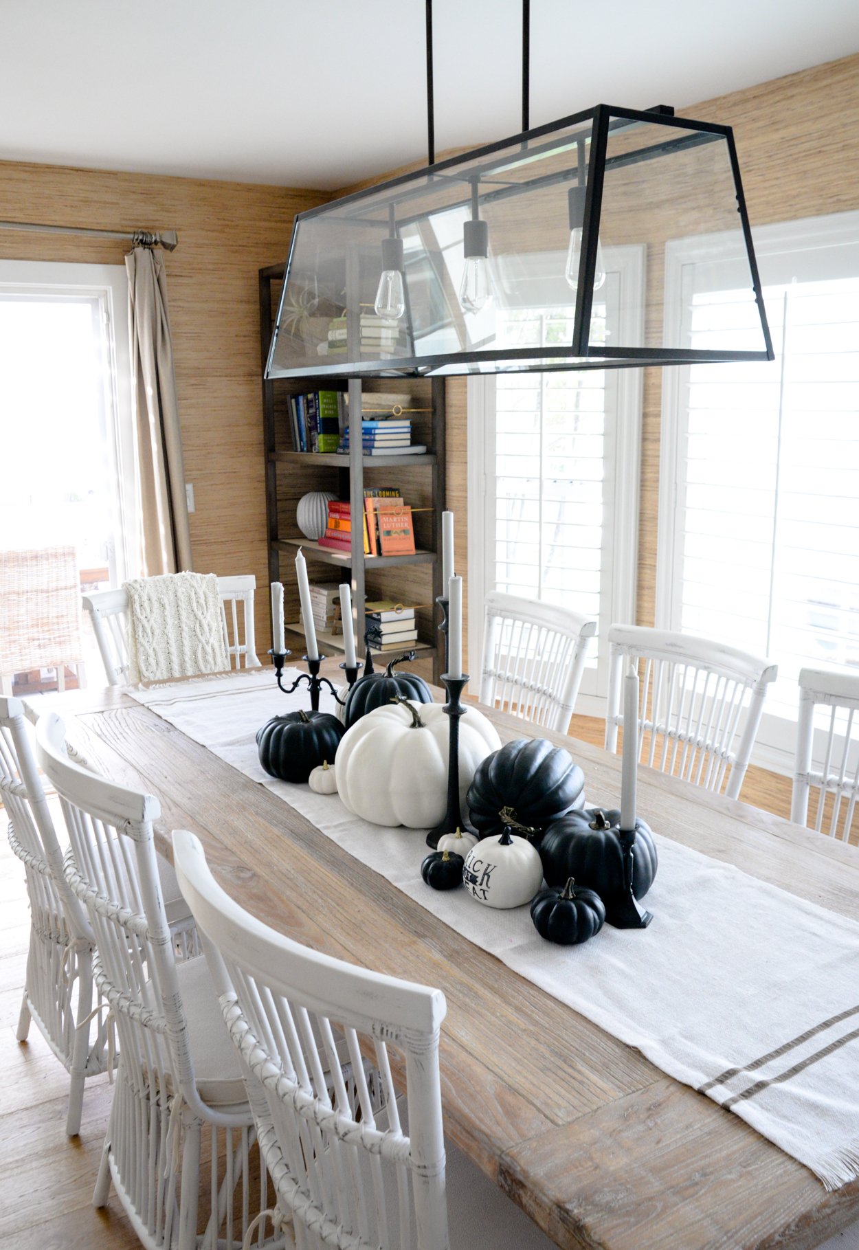 Black and white pumpkins sitting on a rustic wood dining table with white chairs and black candlesticks