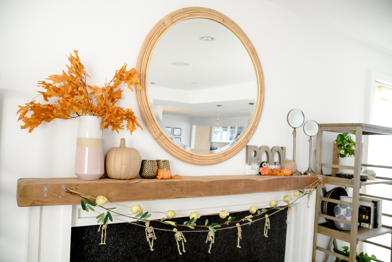 Skull and skeleton garland hanging from a wood beamed mantel with orange leaves and pumpkins and round mirror