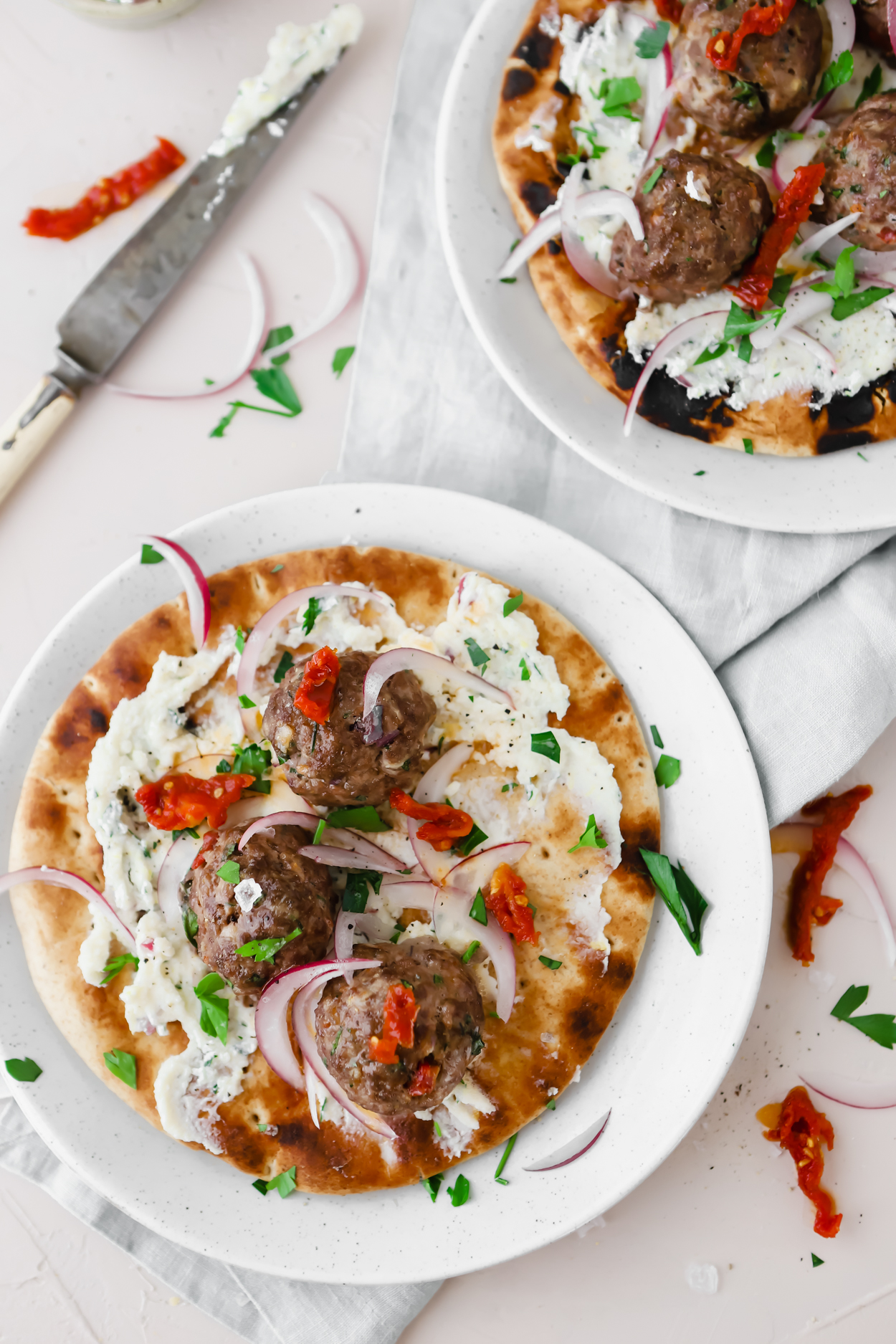 2 baked meatball pita wraps on a white surface garnished with sundried tomatoes and ricotta cheese spread